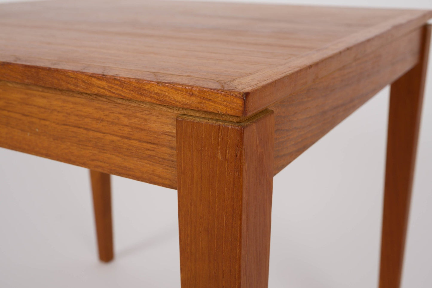 Close-up of mid-century modern Bent Silberg teak nesting table corner with tapered leg and warm wood finish
