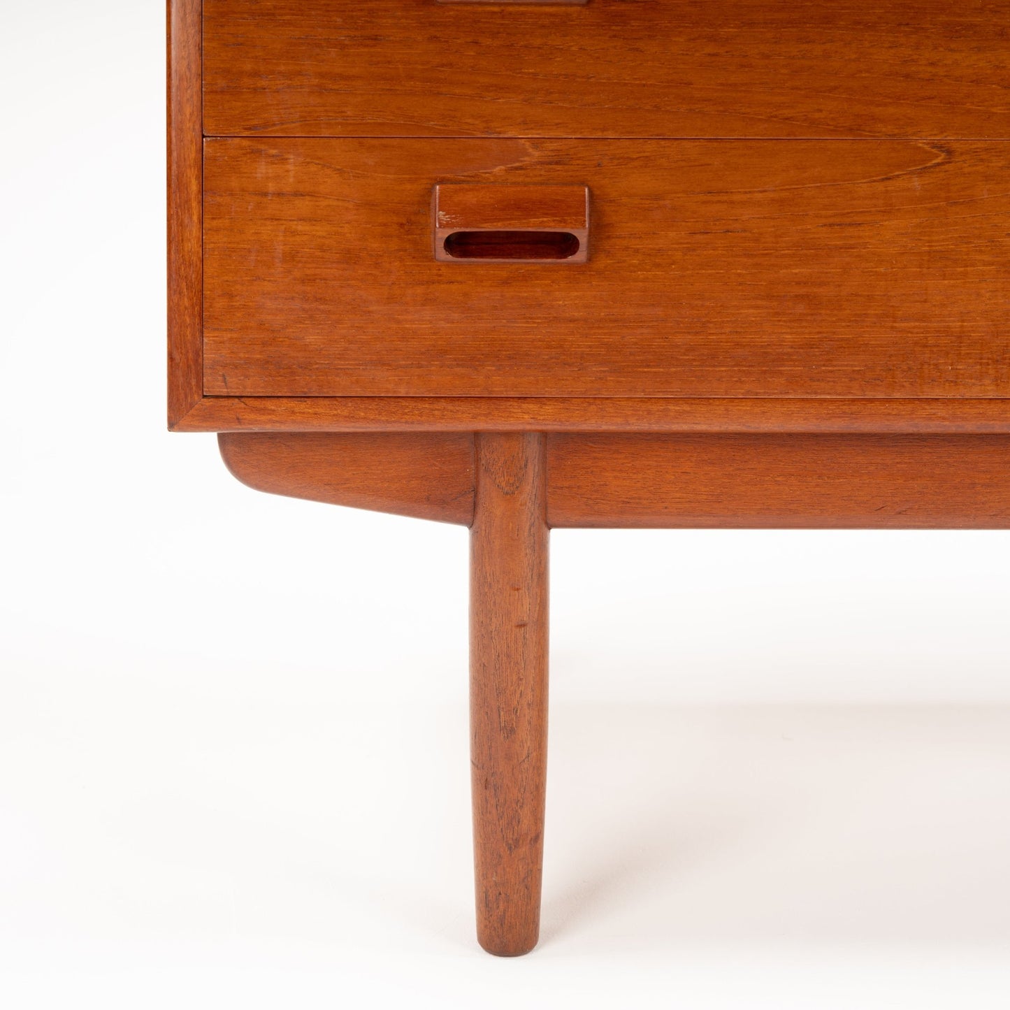 Close-up of mid-century wooden furniture leg and drawer with oval recessed handle in warm teak finish