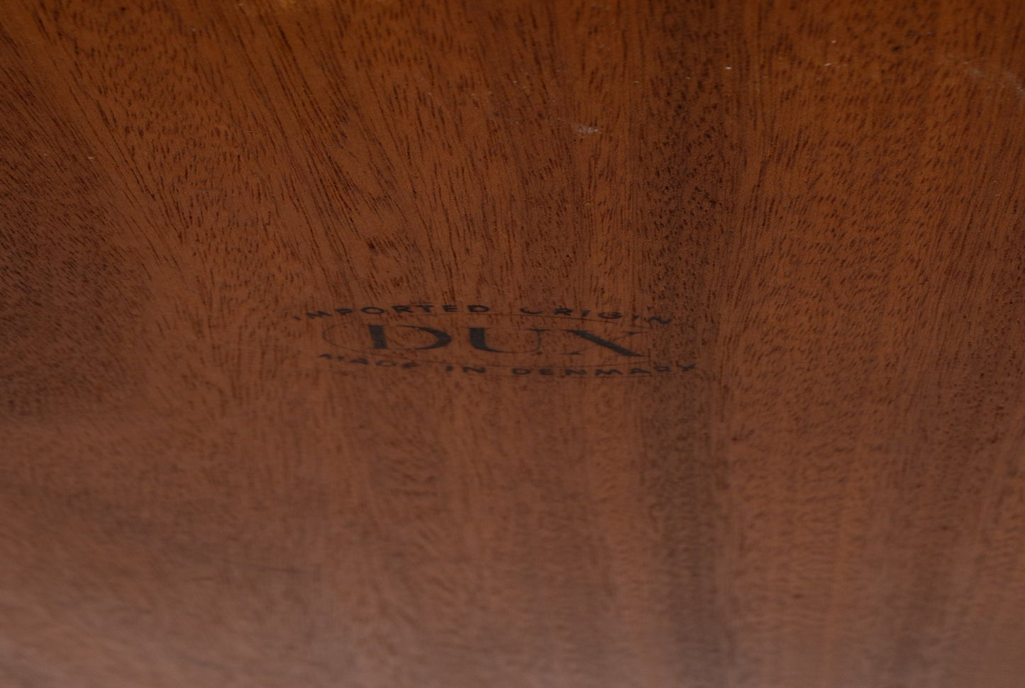 Close-up of stamped DUX logo on the underside of a teak coffee table showcasing wood grain detail.