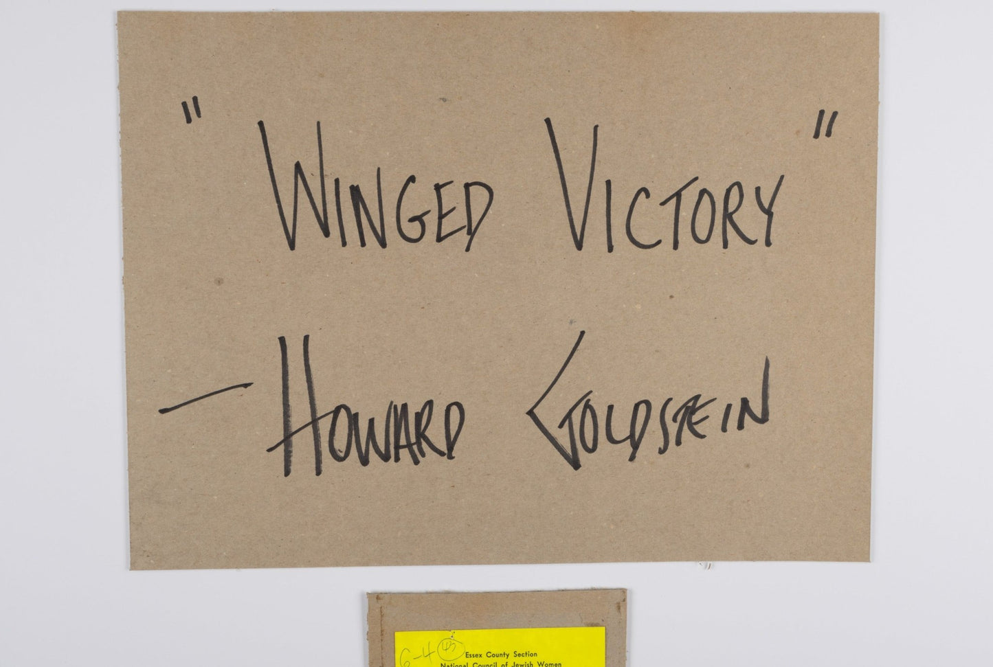 Handwritten title and signature on brown paper reading Winged Victory by Howard Goldstein on white background