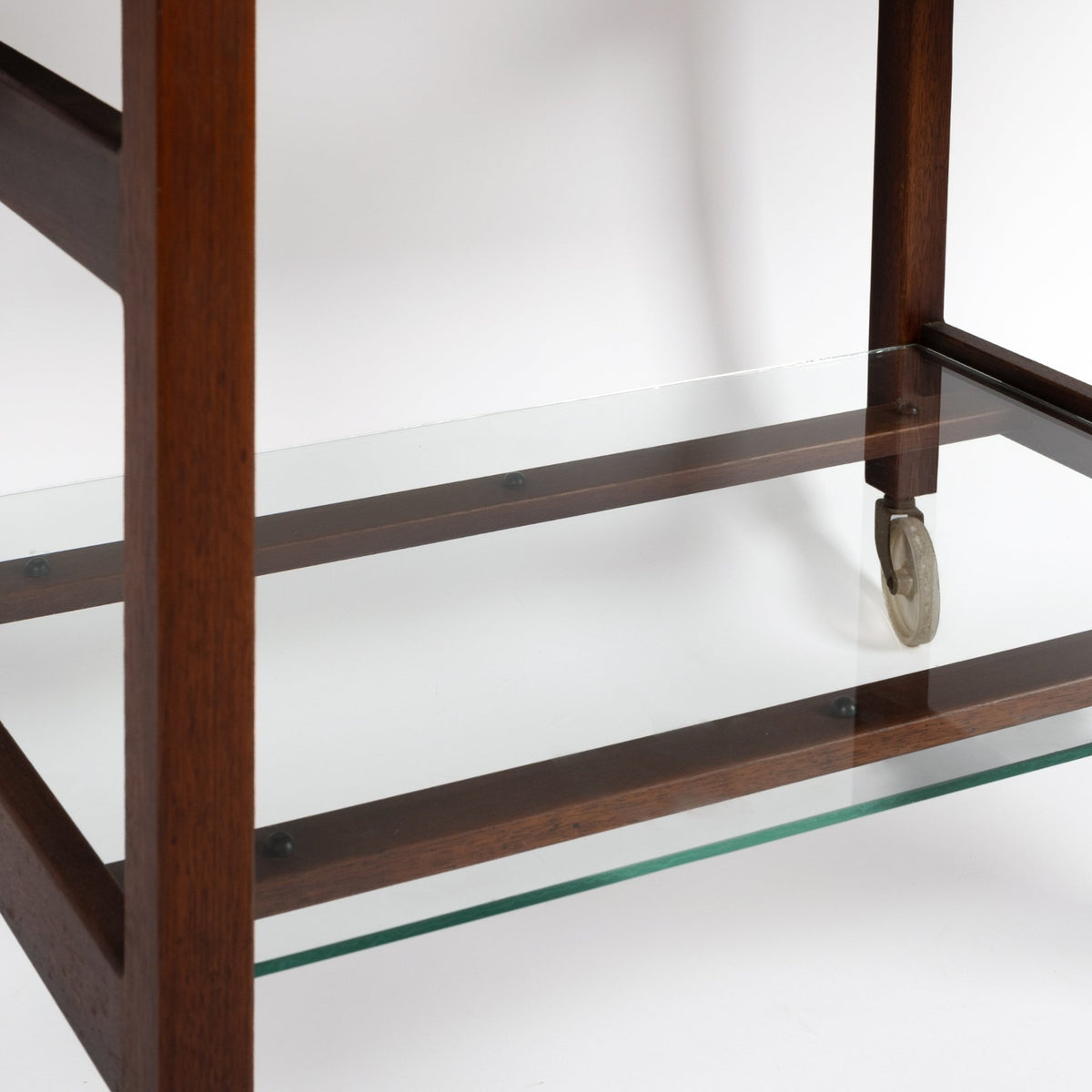 Jens Risom Expandable Serving Cart closeup showing dark walnut frame clear glass shelf and caster against a white background for vintage Danish furniture