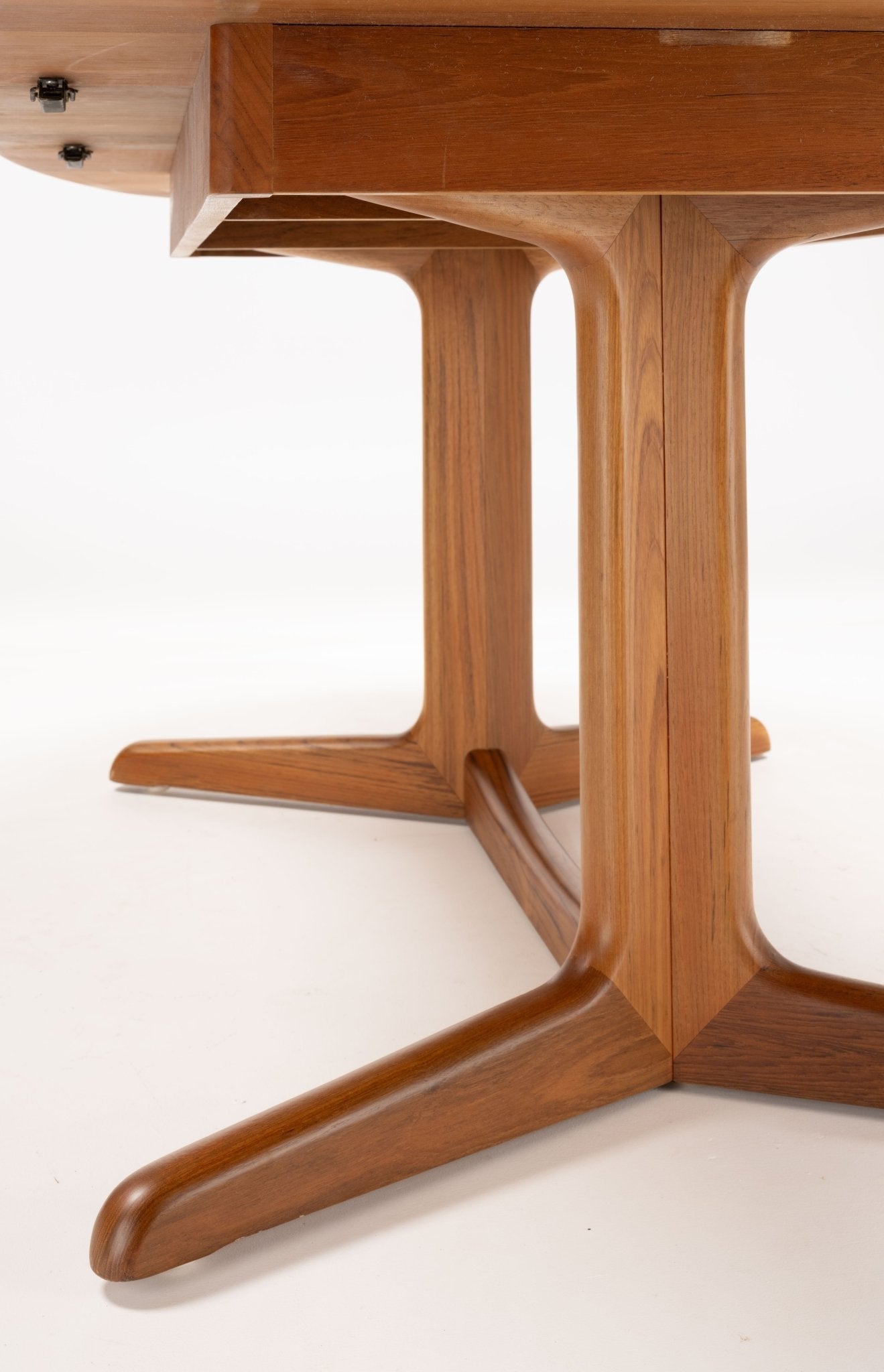 Close-up of mid-century modern teak dining table legs with smooth curved design and warm wood finish on white background