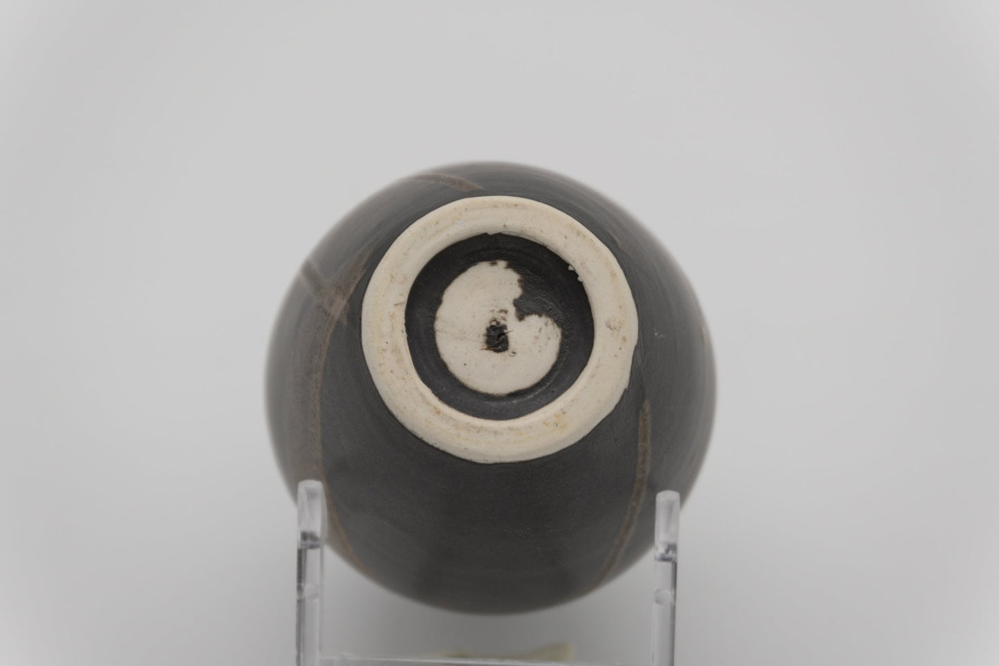 Bottom view of a dark glazed ceramic brush marked vase resting on a clear display stand