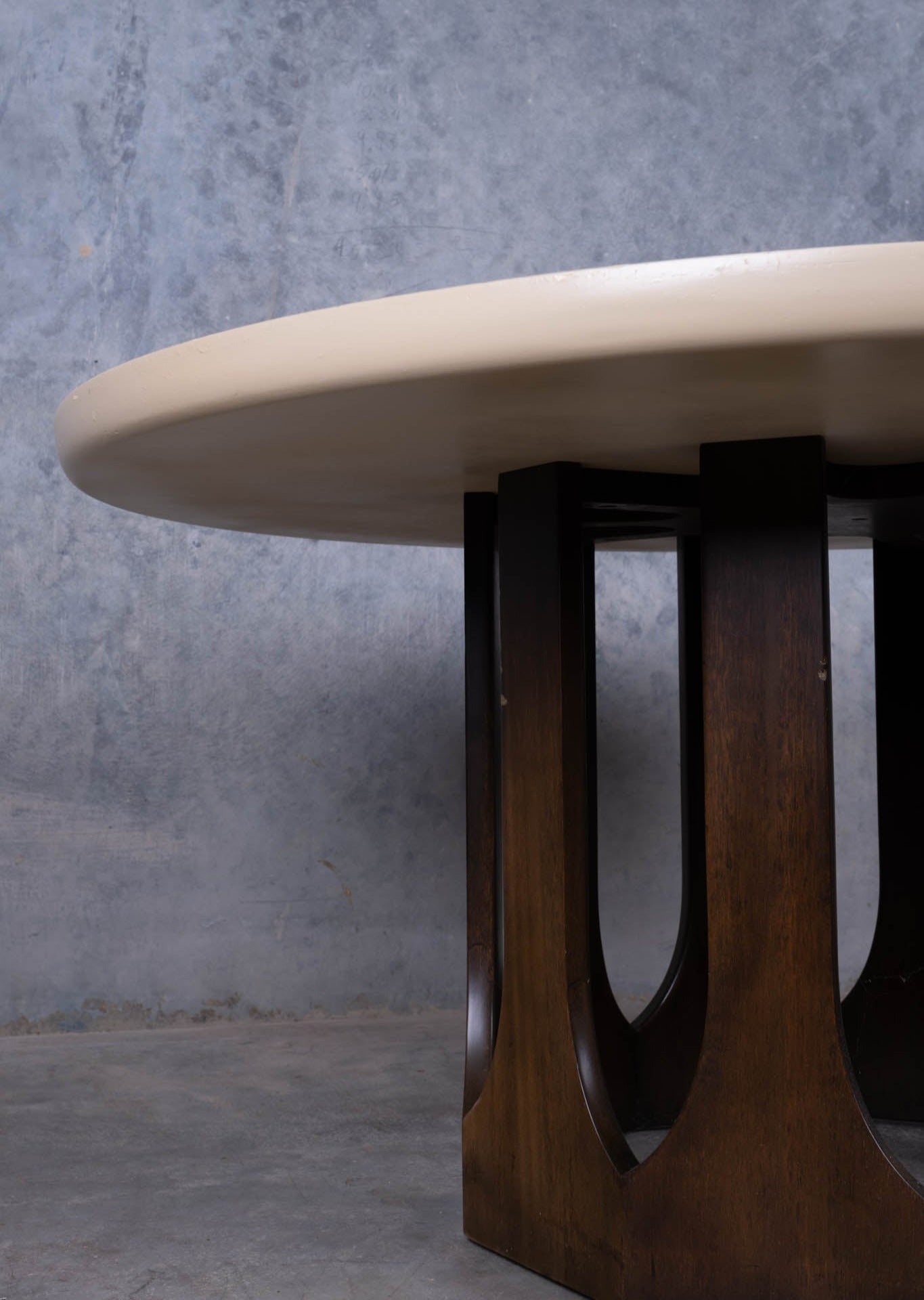 1960s Harvey Probber circular travertine coffee table with carved mahogany arcade base against gray wall background