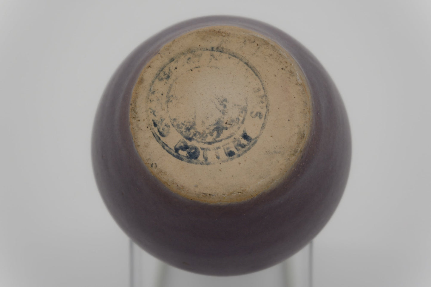 Bottom view of small purple pottery vase with partial maker's mark on unglazed base and smooth glazed surface