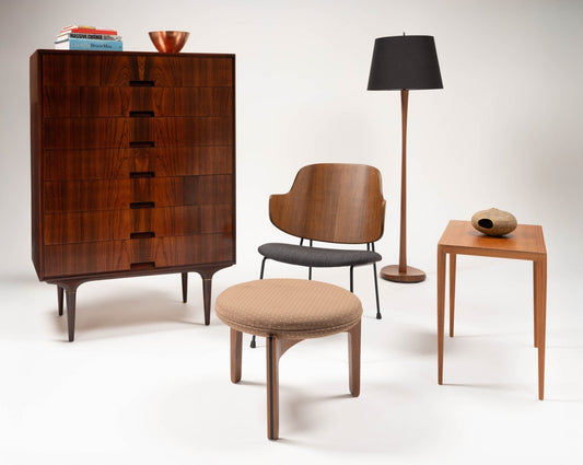 A collection of mid-century modern furniture with a wooden dresser, armchair, lamp, round ottoman, and side table on a white background, conveying elegance and simplicity.