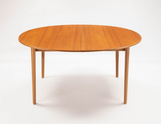 Mid-century modern round teak dining table with tapered legs and a smooth wood grain surface, shown in a compact expandable design suitable for small spaces.