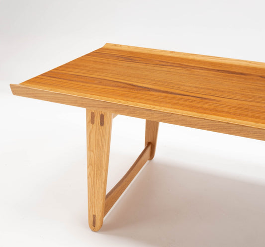 Wooden table with a smooth, polished surface featuring natural grain patterns. It stands on angled legs with a connecting beam, set against a white background.
