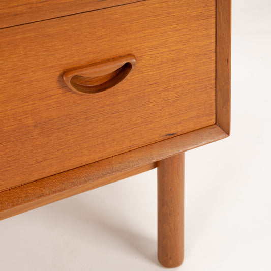 Close-up of a Danish mid century modern teak cabinet featuring a sculpted recessed drawer pull, beautifully figured teak grain, clean case construction, and solid round tapered legs