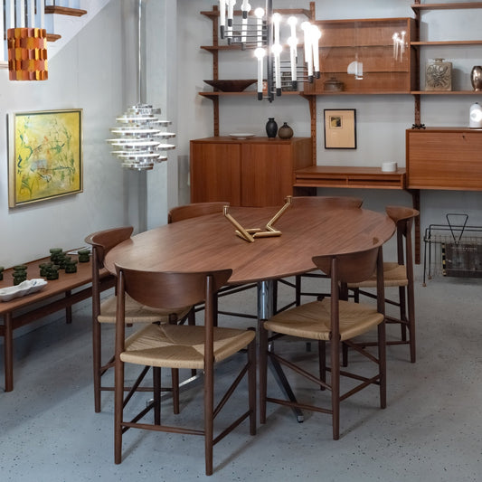 Mid-century modern dining room with a wooden oval table, six chairs, and a brass centerpiece.