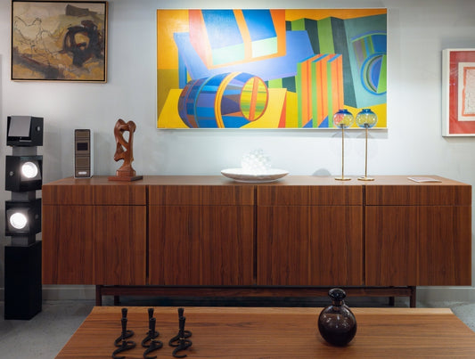Mid-century modern teak credenza and coffee on display inside a retail store. Next to it is a lamp and multiple paintings.
