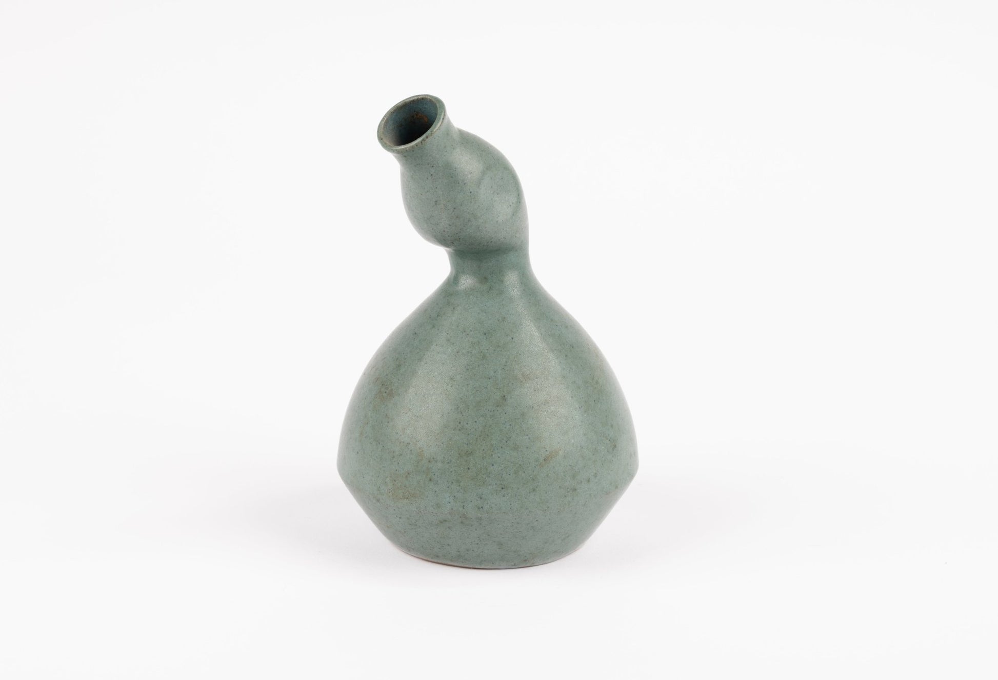 Abstract celadon studio pottery vase with gently swelling body and tilted neck, hand-formed ceramic on white background