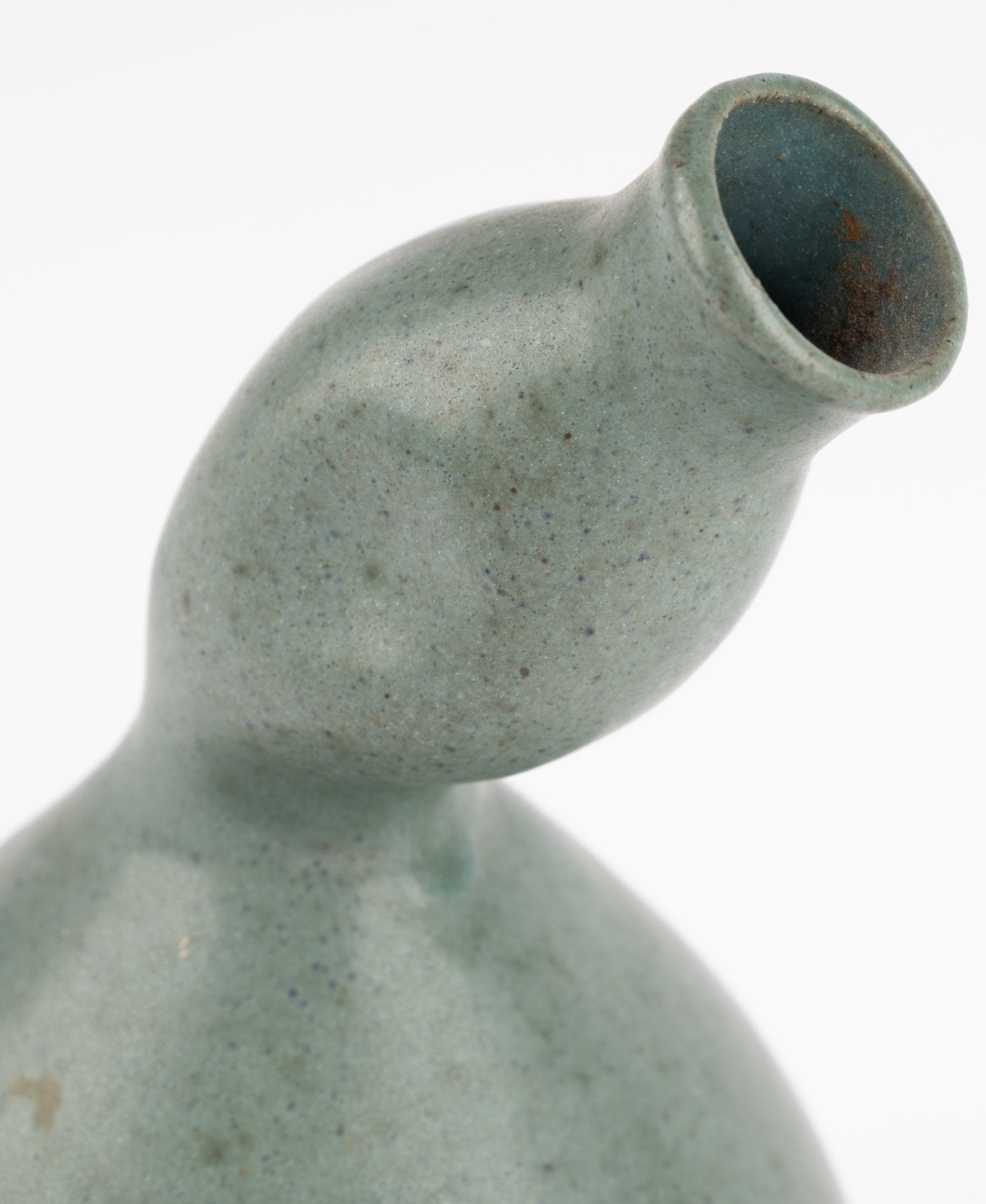 Close-up of abstract celadon studio pottery vase with gently swelling body and tilted neck on white background