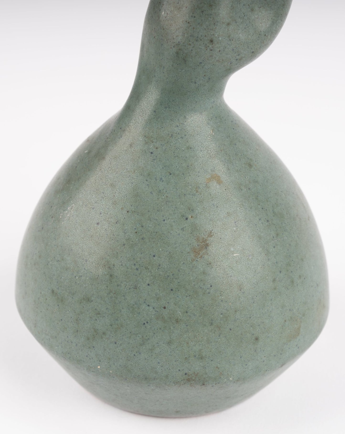 Close-up of abstract celadon studio pottery vase with gently swelling body and soft green glaze on white background