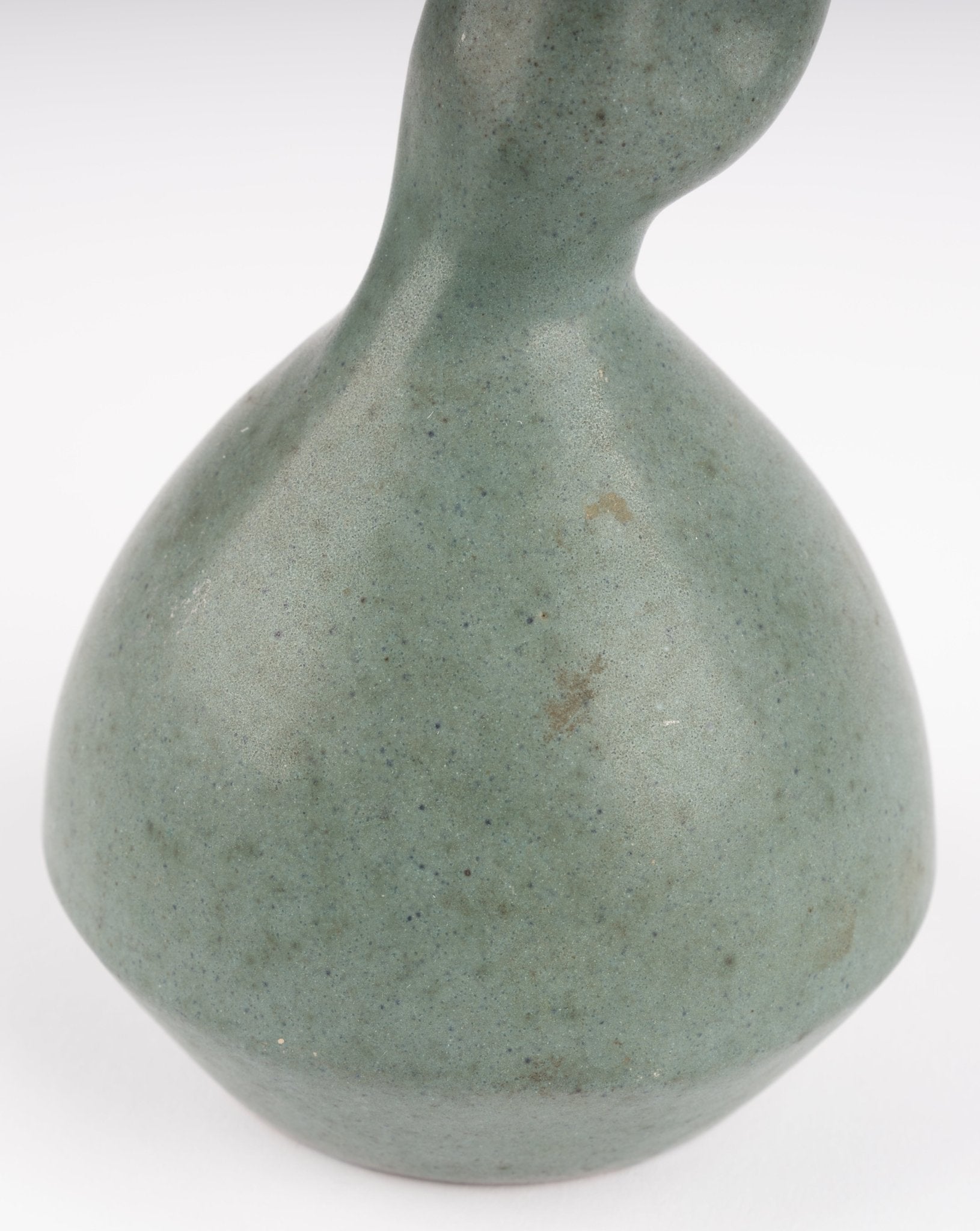 Close-up of abstract celadon studio pottery vase with gently swelling body and soft green glaze on white background