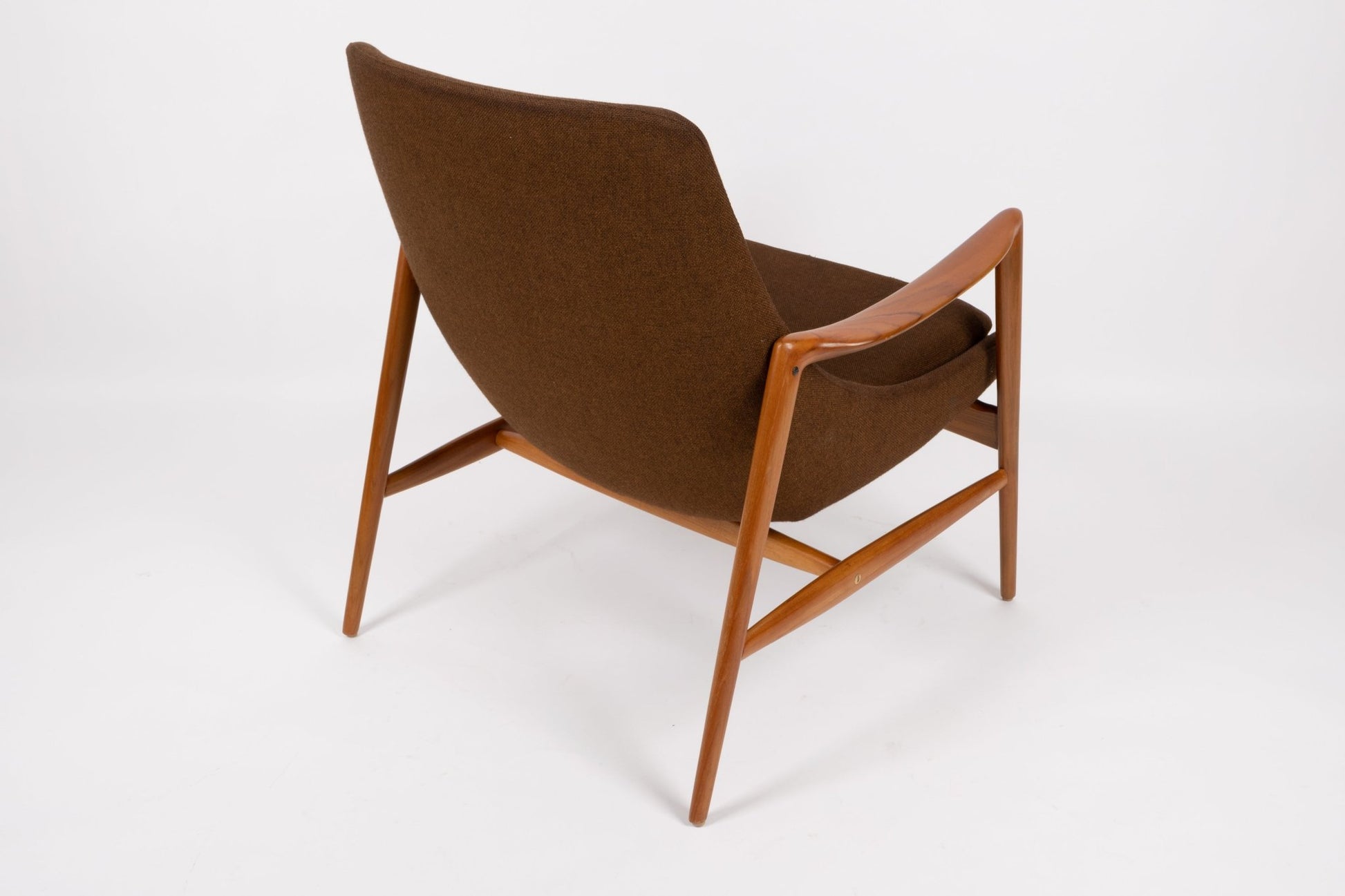 Mid-century modern lounge chair with sculptural teak frame and brown wool upholstery angled view on white background