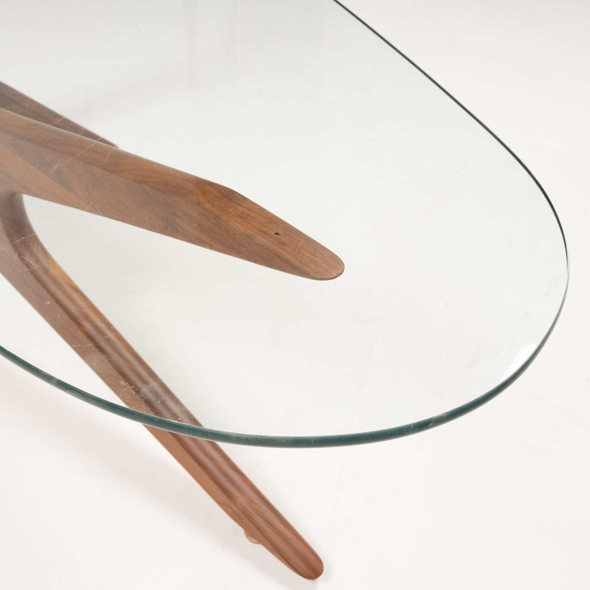 Curved clear glass top with sculptural solid walnut base featuring three tapered legs in jack-inspired design