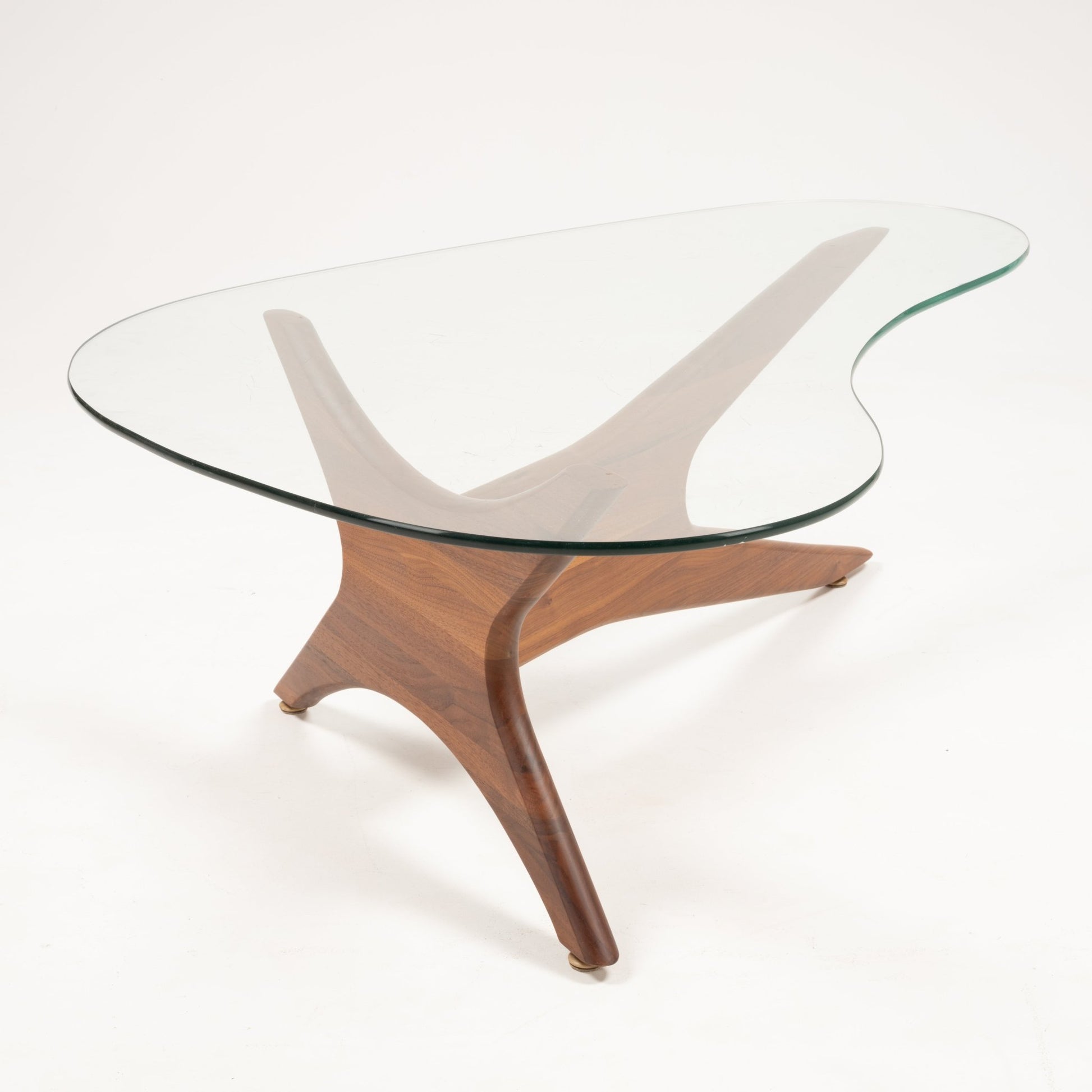 Asymmetrical glass top coffee table with three-legged sculptural solid walnut base on white background