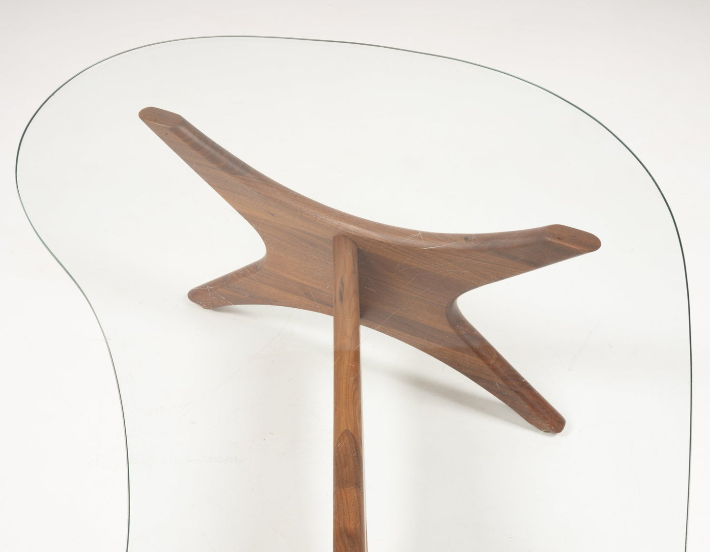 Kidney-shaped clear glass top supported by sculptural solid walnut base with three extended legs in organic design