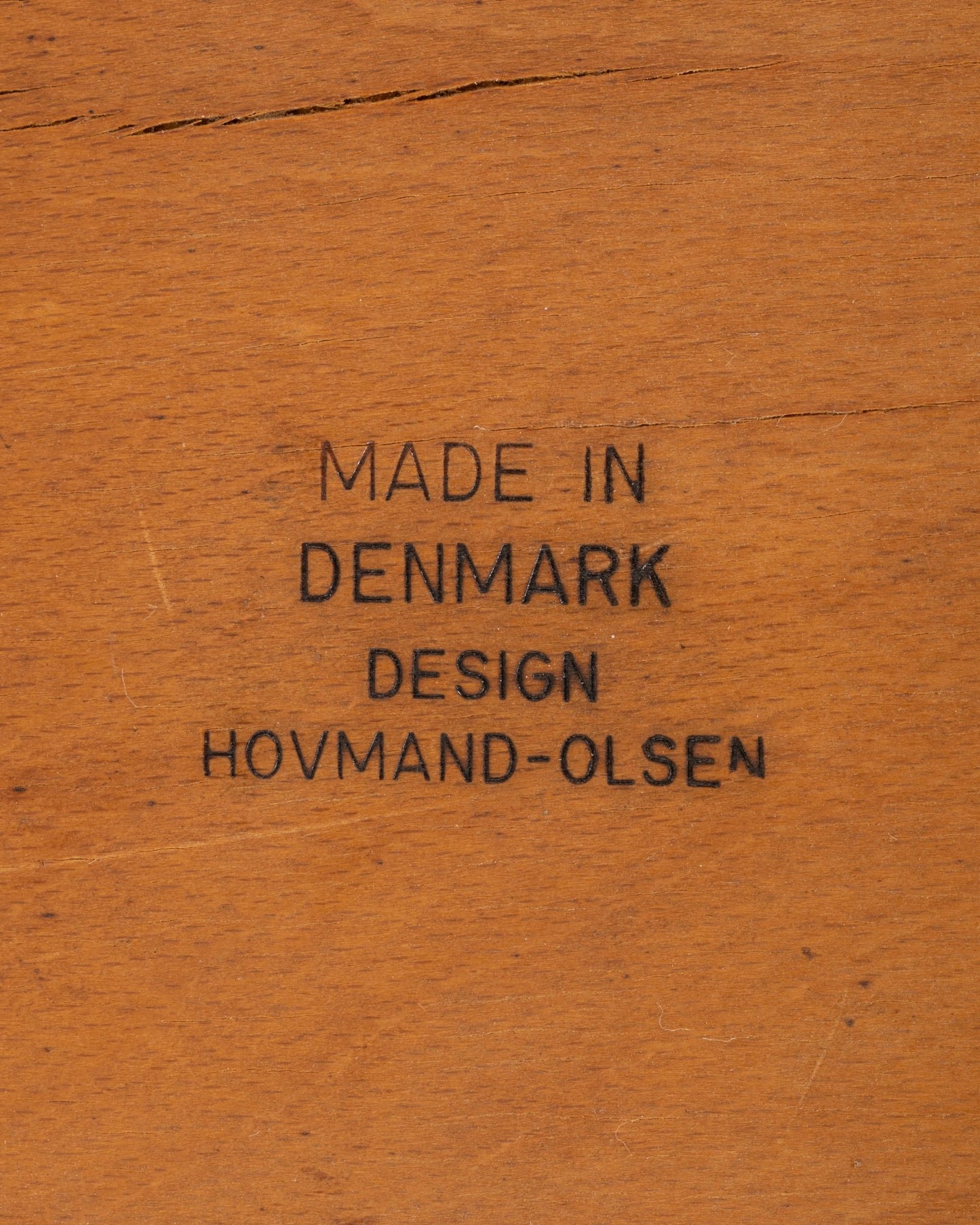 Close-up of wood stamp marking "Made in Denmark Design Hovmand-Olsen" on vintage teak chair component.