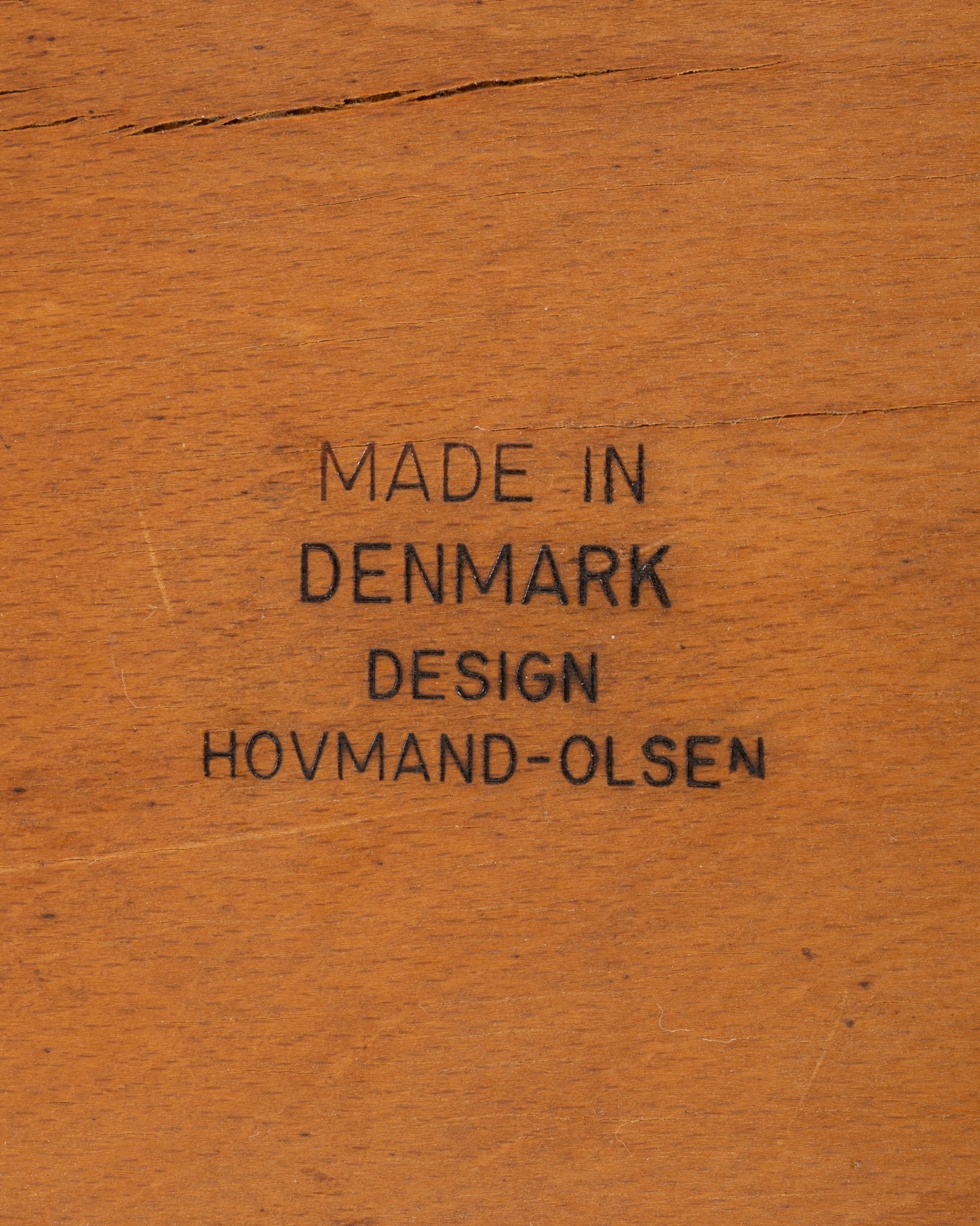 Close-up of wood stamp marking "Made in Denmark Design Hovmand-Olsen" on vintage teak chair component.