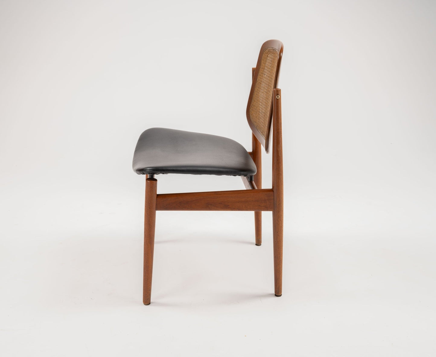 Side view of mid-century modern Arne Vodder dining chair with teak frame, cane backrest, and black leather seat cushion.
