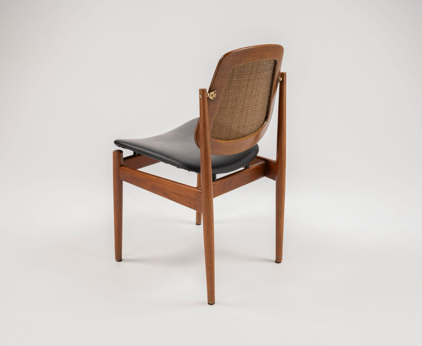 Mid-century modern Arne Vodder teak dining chair with woven backrest, hinged brass fittings, and black leather seat.