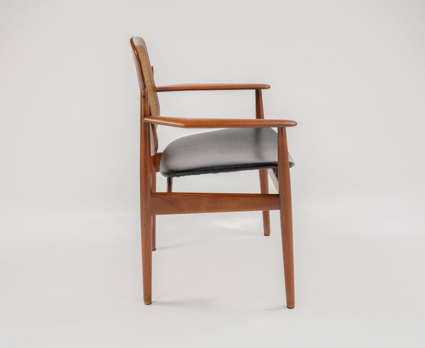 Side view of mid-century modern Arne Vodder teak dining chair with sculpted frame and black upholstered seat
