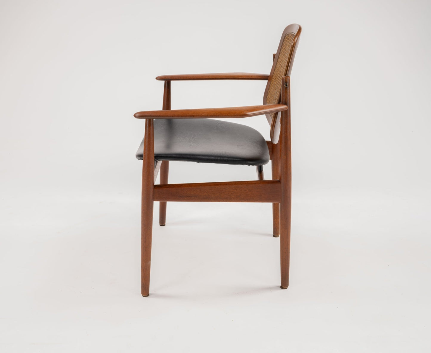 Side view of mid-century modern teak dining chair with black leather seat and curved armrests