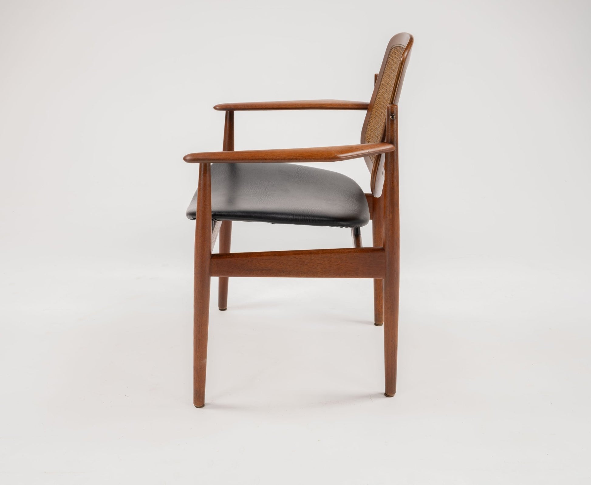 Side view of mid-century modern teak dining chair with black leather seat and curved armrests