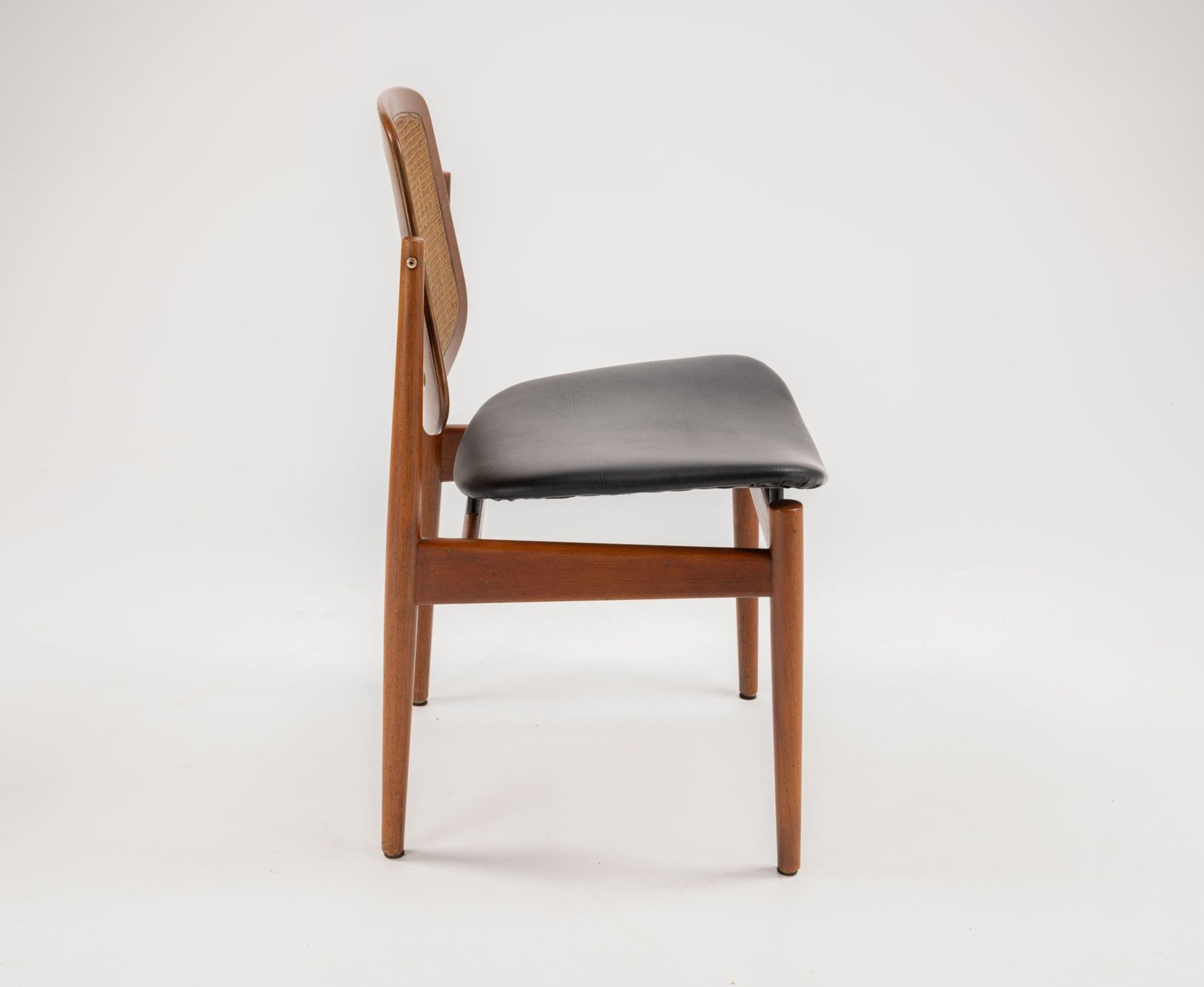 Side view of mid-century modern Arne Vodder teak dining chair with hinged backrest and black leather seat.