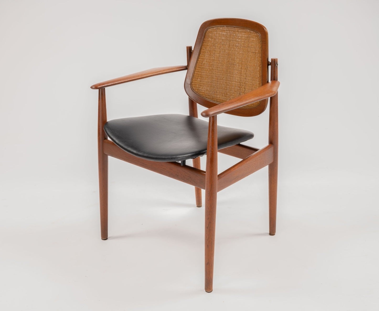 Arne Vodder dining chair with teak frame, caned backrest, hinged brass fittings, and black leather seat cushion.