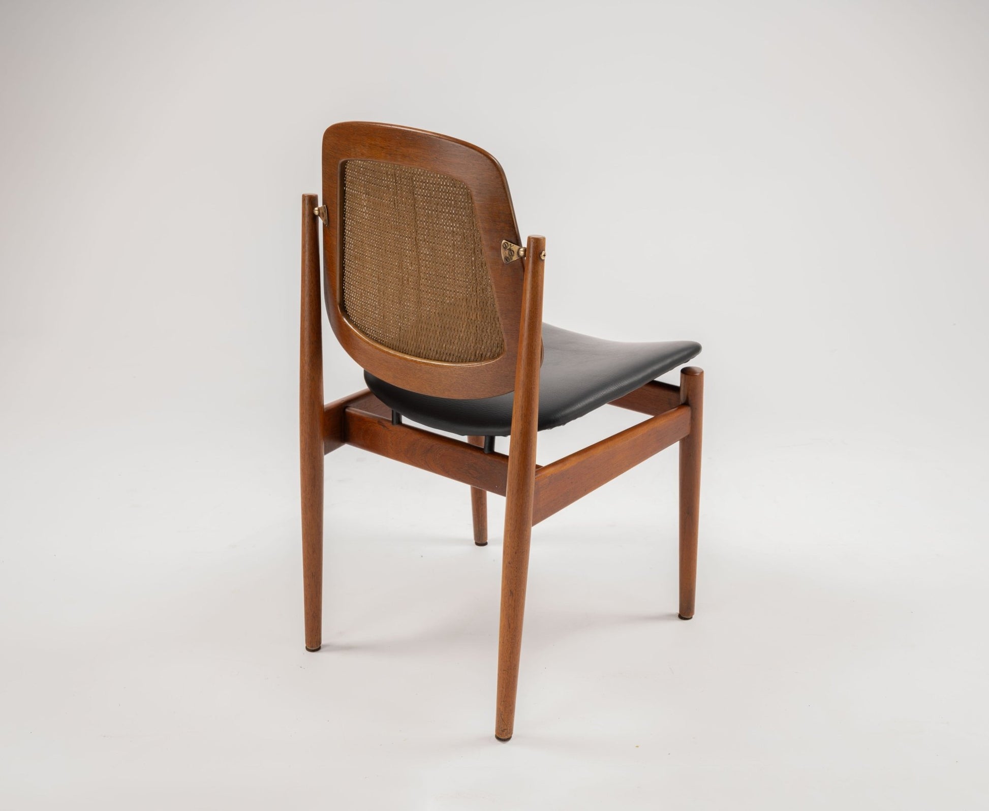 Mid-century modern teak dining chair with curved cane backrest, black leather seat, and brass hardware detailing.