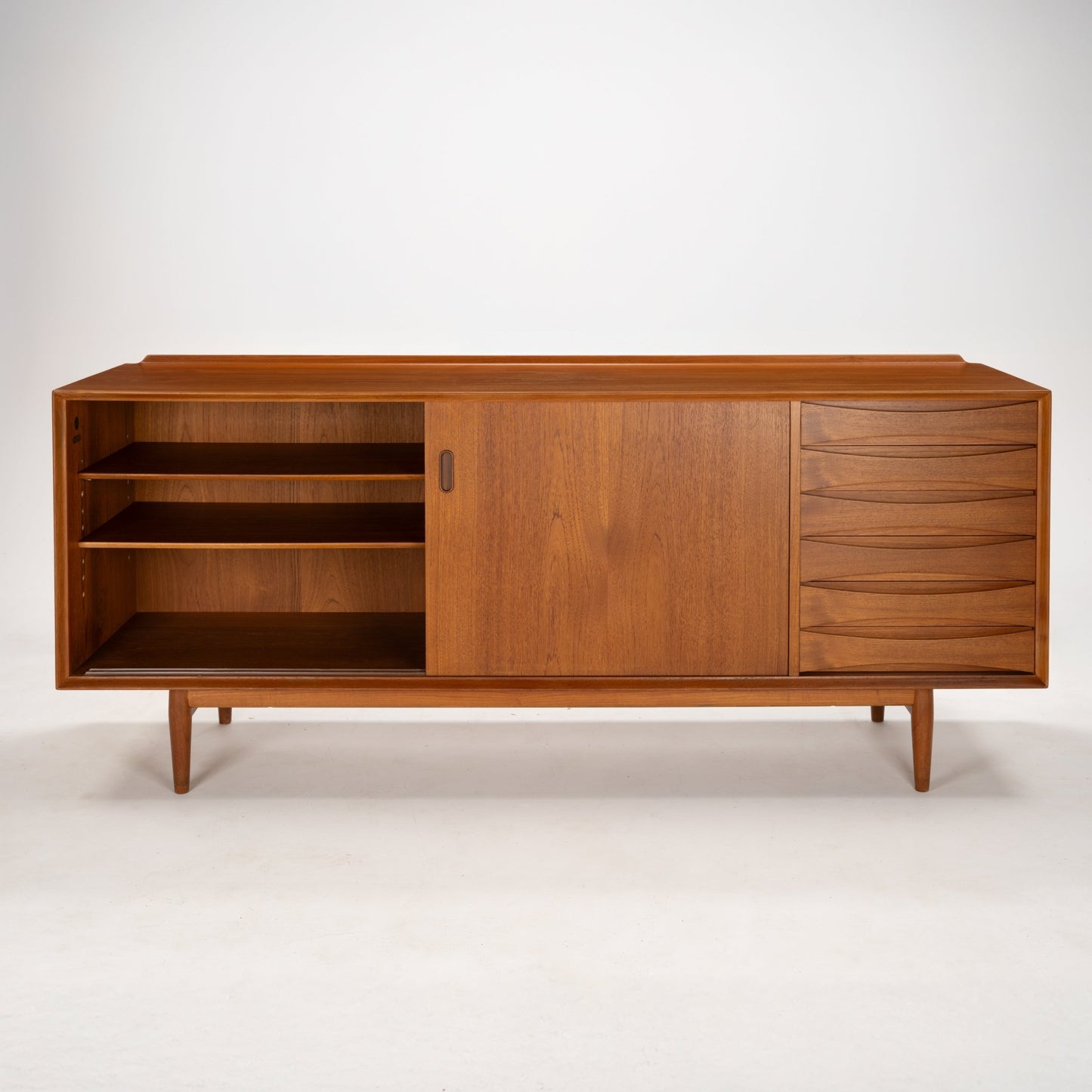 Arne Vodder Reversible-Drawer Teak Credenza for Sibast featuring smooth teak wood with open shelving, a sliding door, and sculpted drawers on tapered legs in mid century modern style.