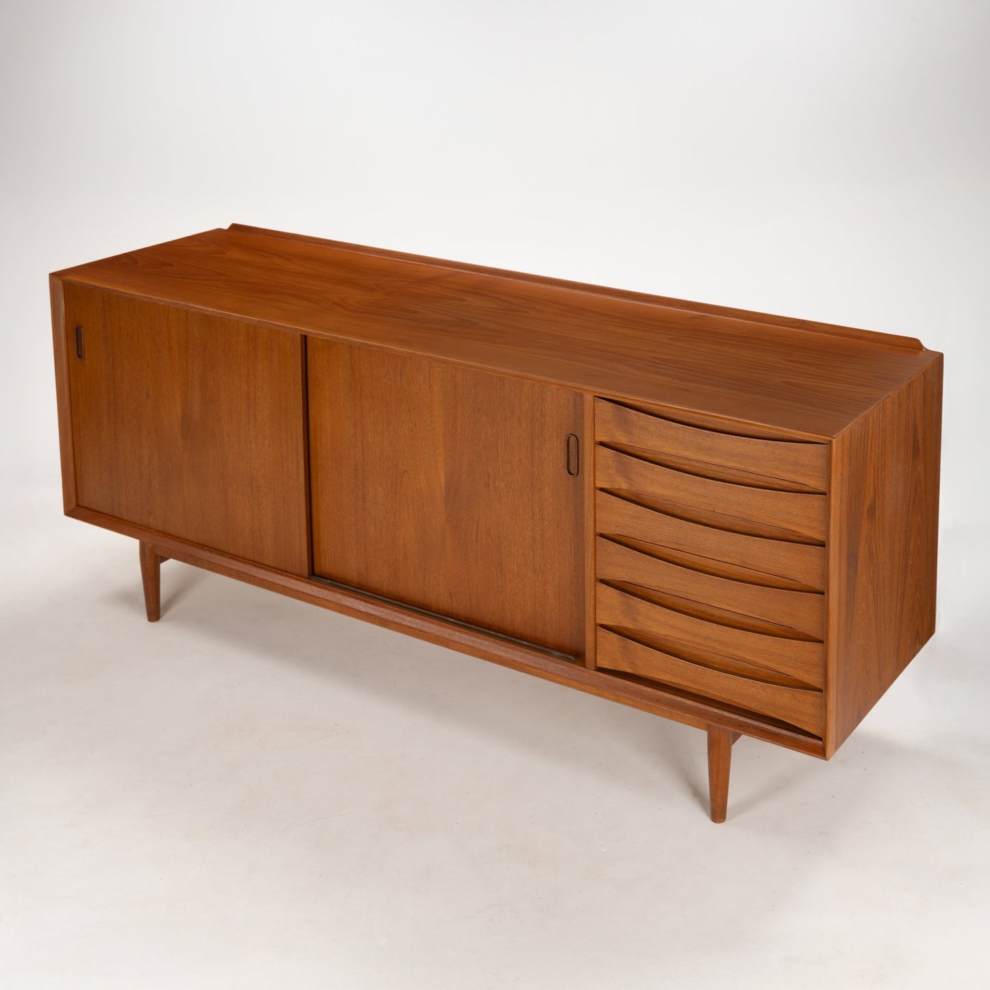 Arne Vodder Reversible-Drawer Teak Credenza for Sibast with warm teak wood, featuring smooth sliding doors and a column of sculpted drawers, elevated on slender tapered legs in mid century modern style.
