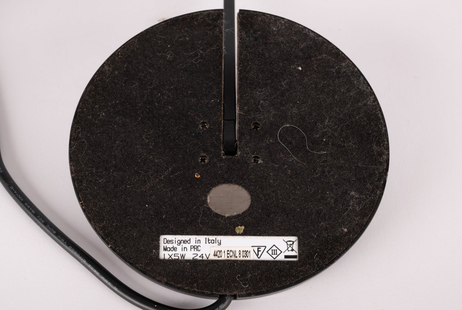 Base of black Artemide Itis table lamp showing sticker with specifications and attached power cord on white background.