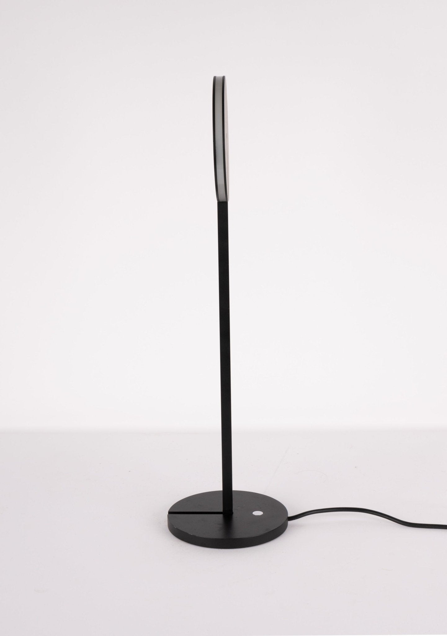 Minimalist black Artemide Itis table lamp with circular base and slim vertical stem against white background