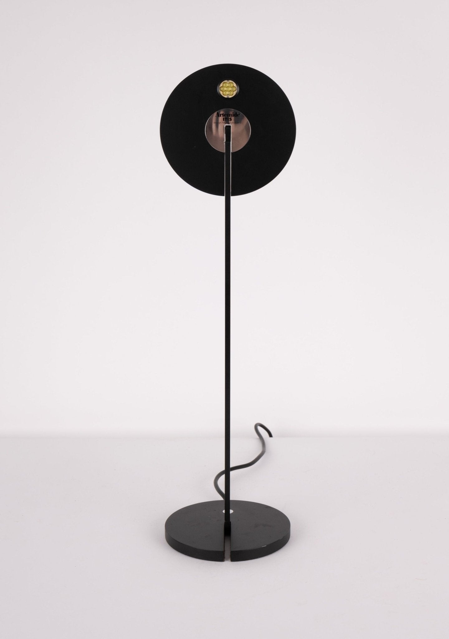 Minimalist black Artemide Itis table lamp with circular base and adjustable arm, LED light source visible from front view.