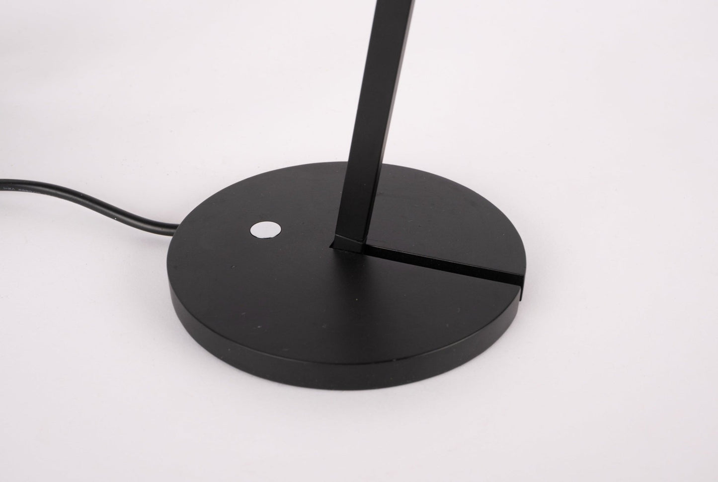 Base of black Artemide Itis table lamp with circular shape and adjustable arm on white background.