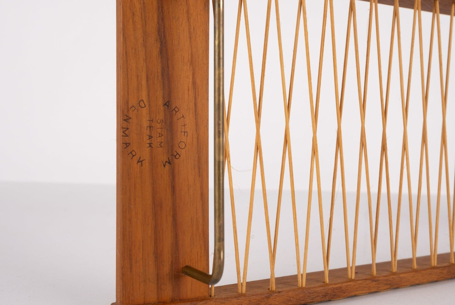 Close-up of Danish 1960s teak bread tray with woven rattan and brass hardware showing manufacturer’s mark.
