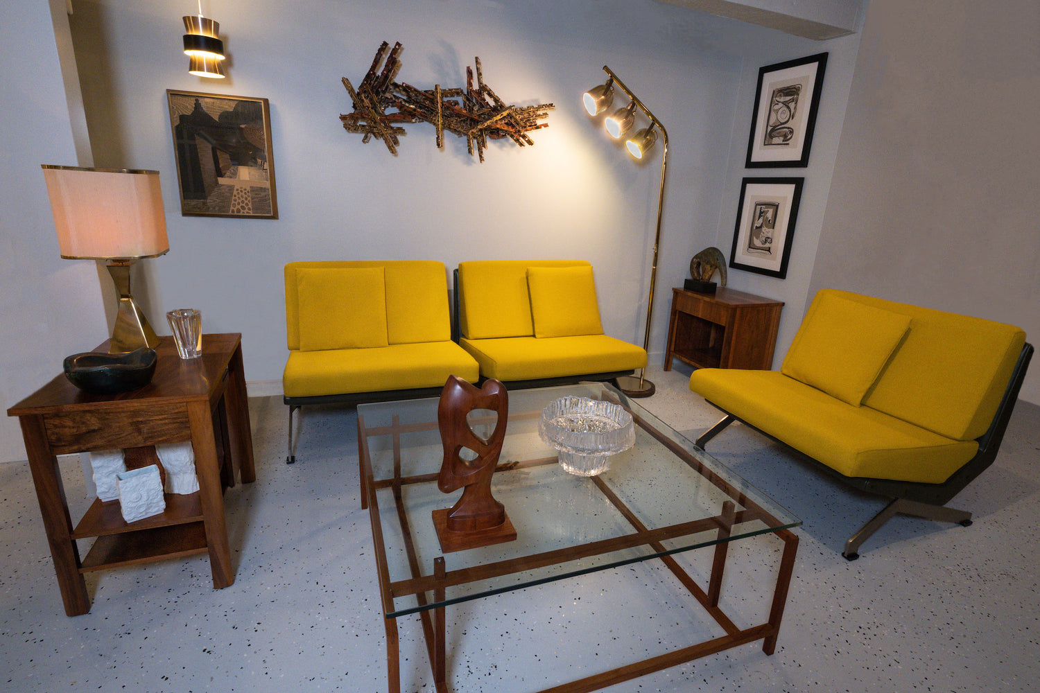 staged furniture setup consisting of three lounge chairs, glass coffee table, floor lamp, side table with table-lamp, and decorative wall objects