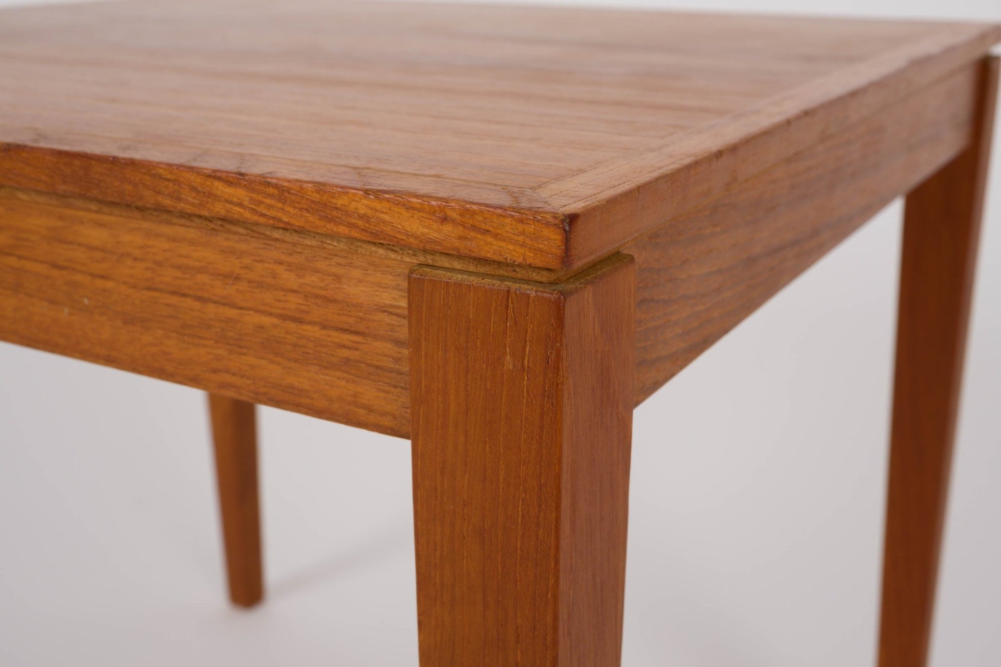 Close-up of mid-century modern Bent Silberg teak nesting table corner with tapered leg and warm wood finish