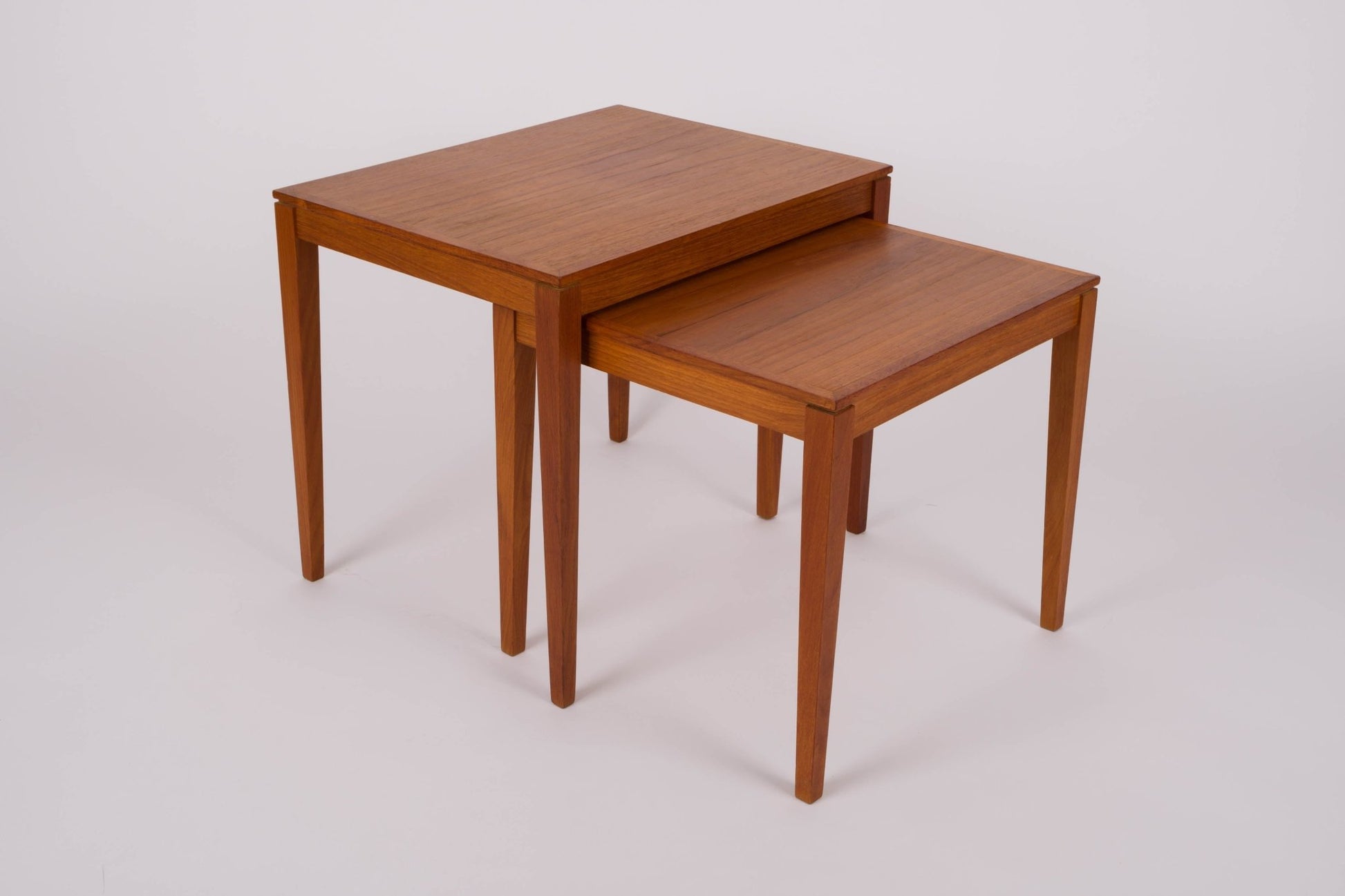 Pair of mid-century modern Bent Silberg teak nesting tables with tapered legs and clean lines on plain background