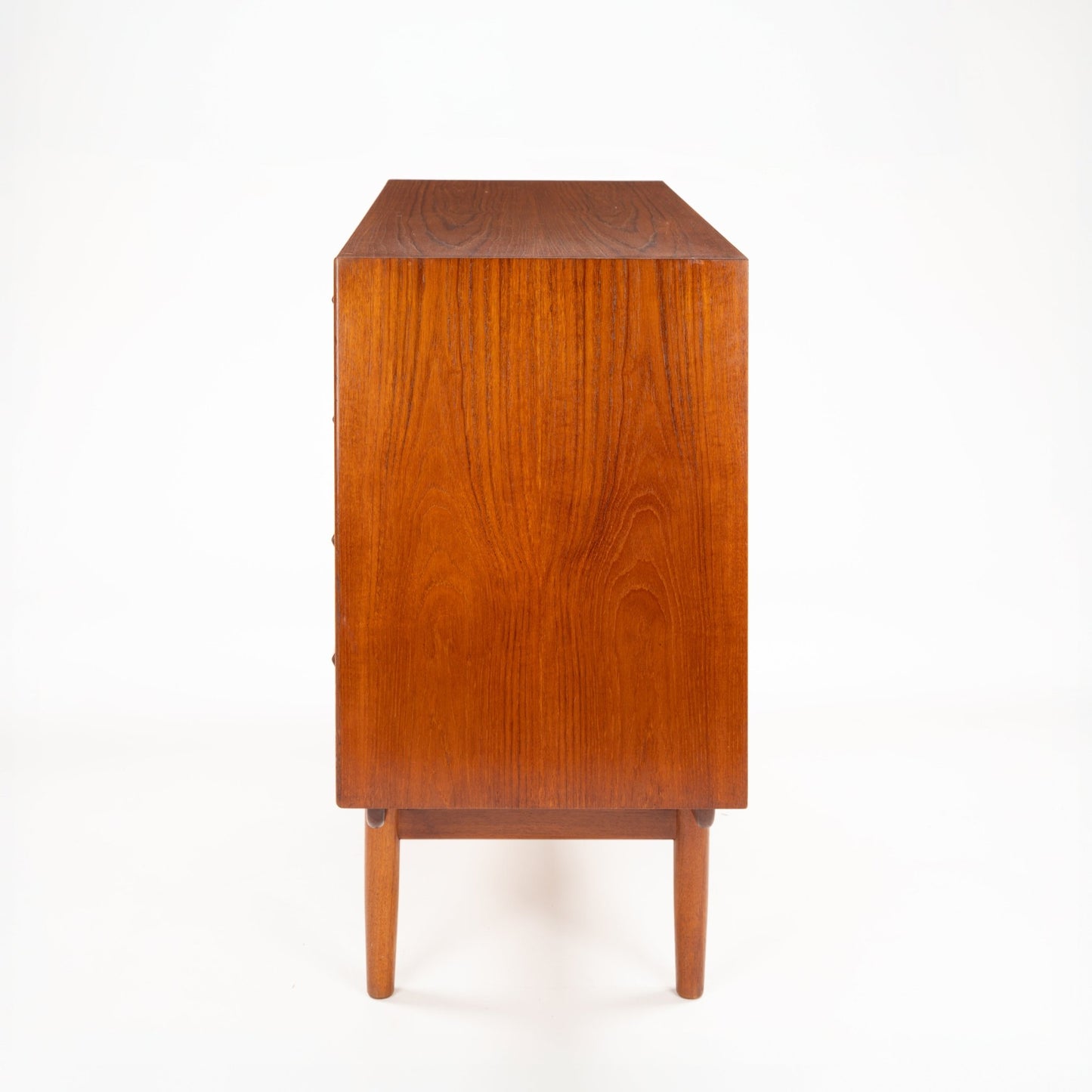 Side view of a mid-century wooden dresser showcasing warm wood grain and tapered legs against white background