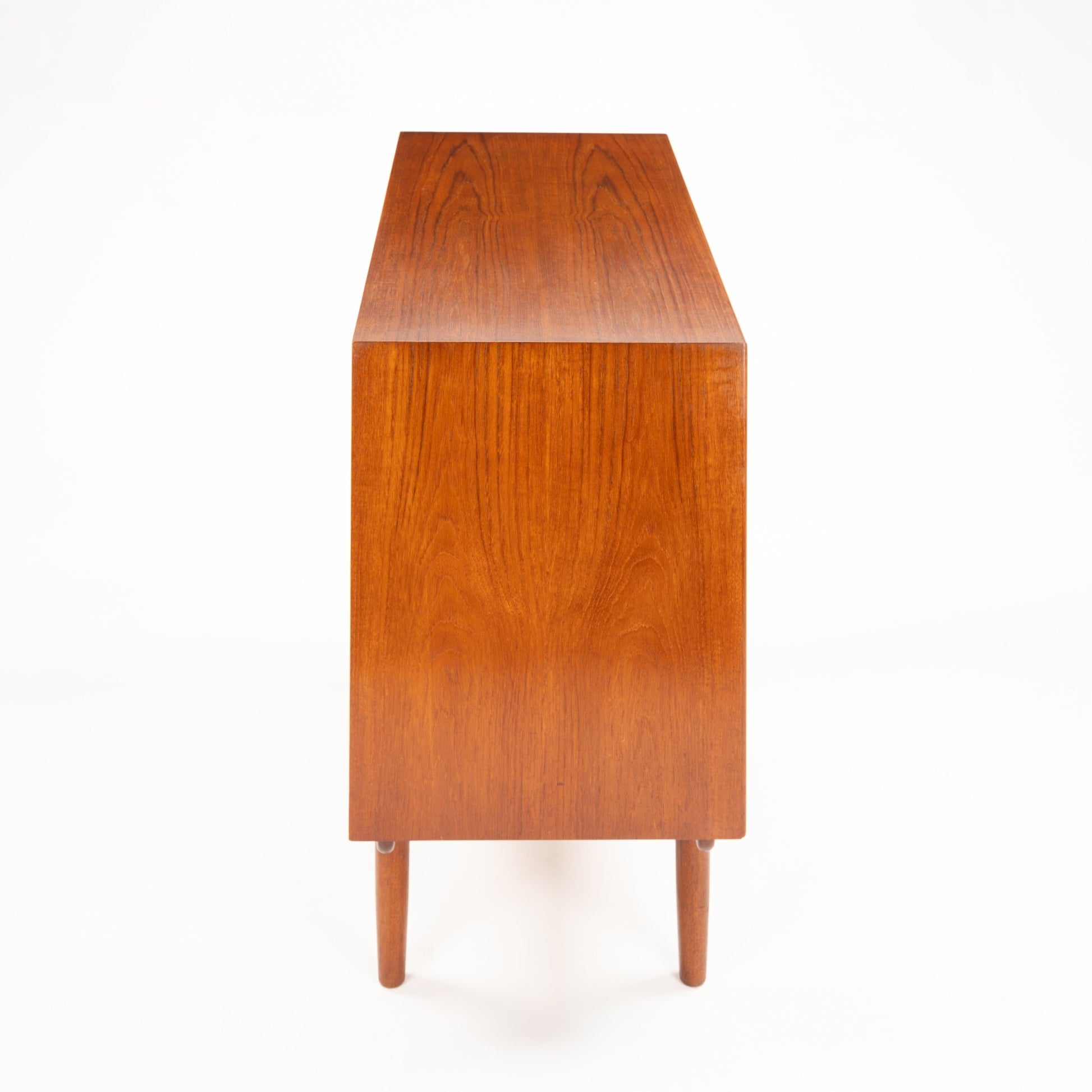 Side profile of mid-century wooden dresser with tapered legs and warm natural wood grain finish