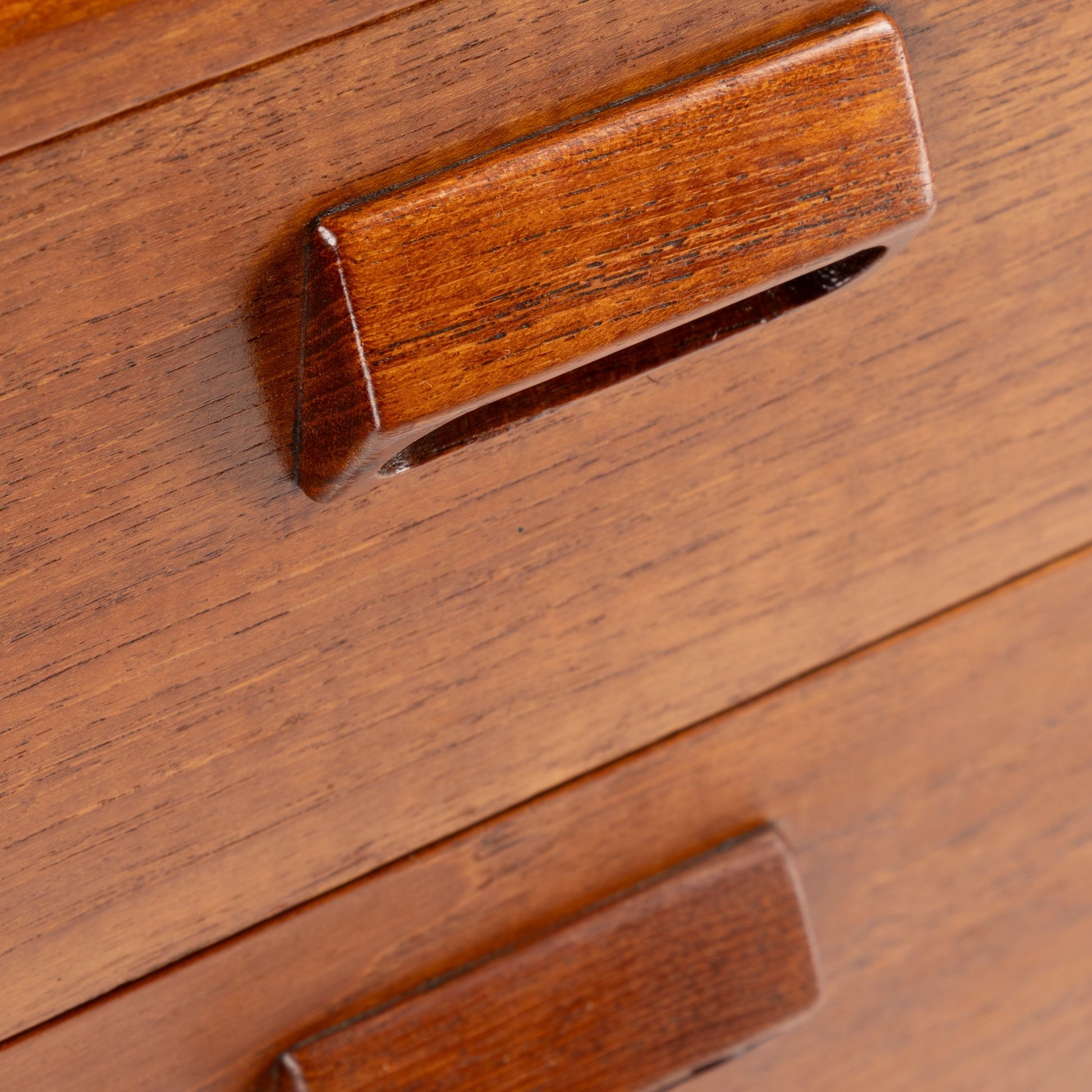 Close-up of wooden dresser drawers featuring angled recessed handles with rich warm wood grain finish