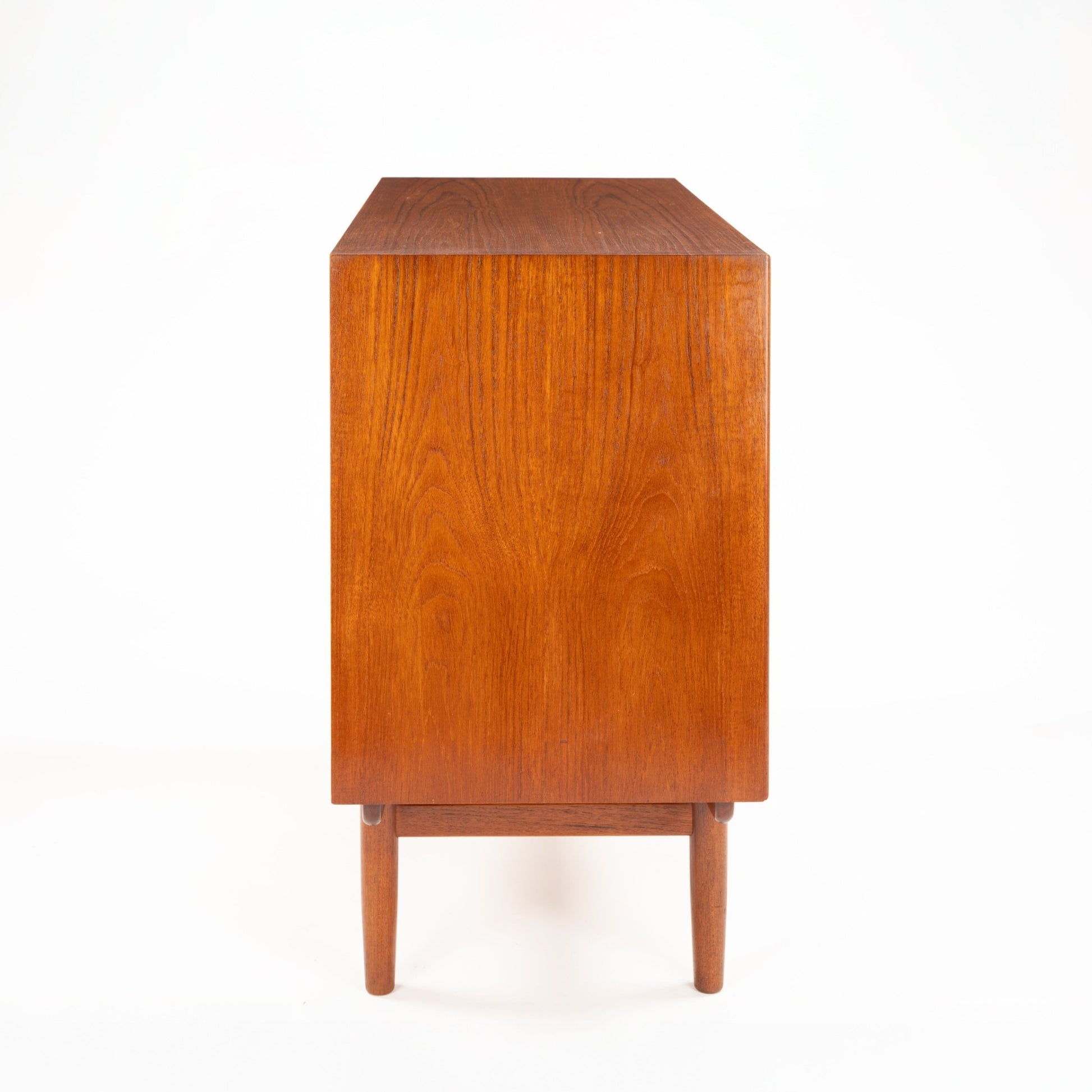 Side view of mid-century wooden cabinet with warm wood veneer and slender tapered legs against white background