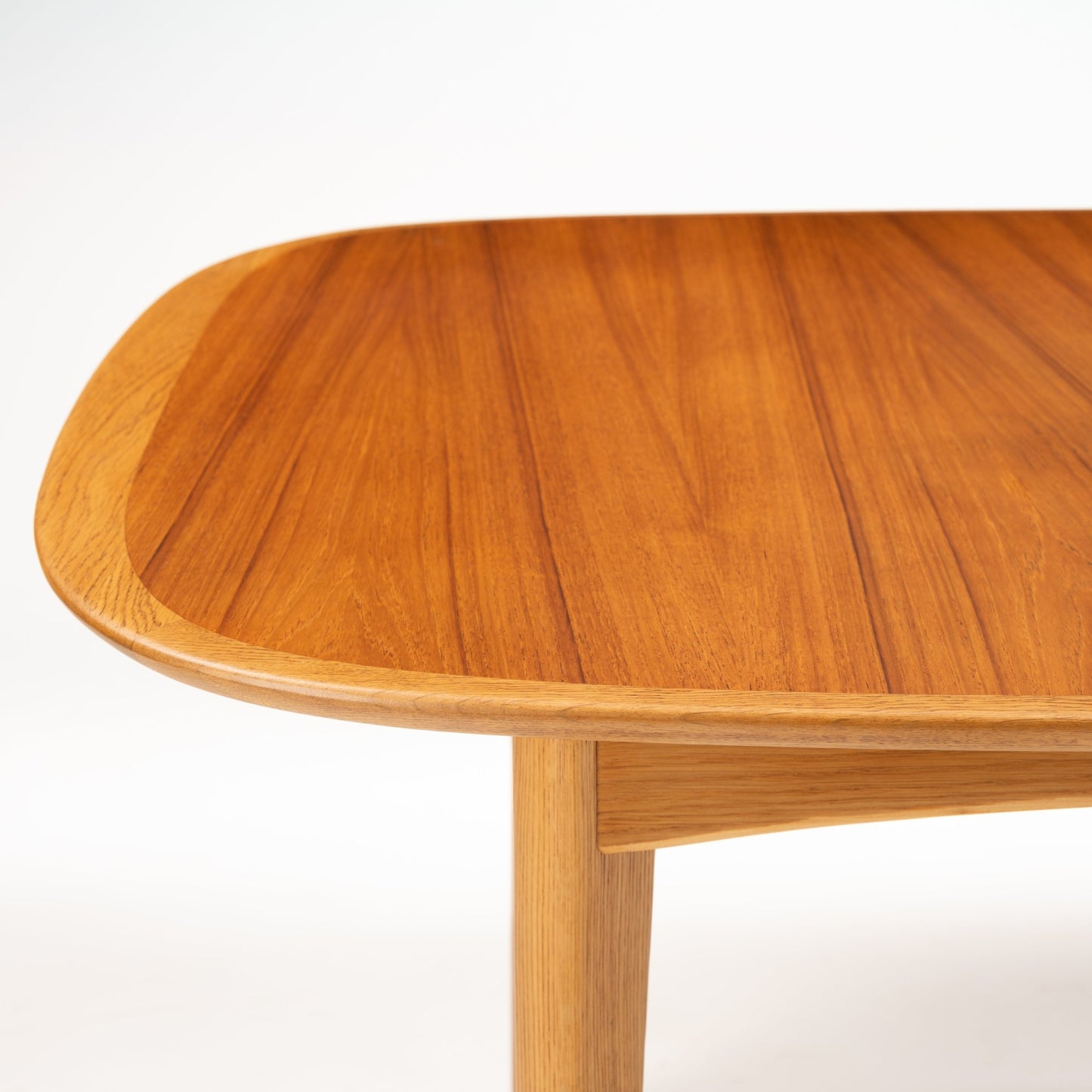Danish Butterfly-Leaf Teak Dining Table closeup with rounded edge tabletop warm teak grain tapered leg and apron in vintage Danish furniture style