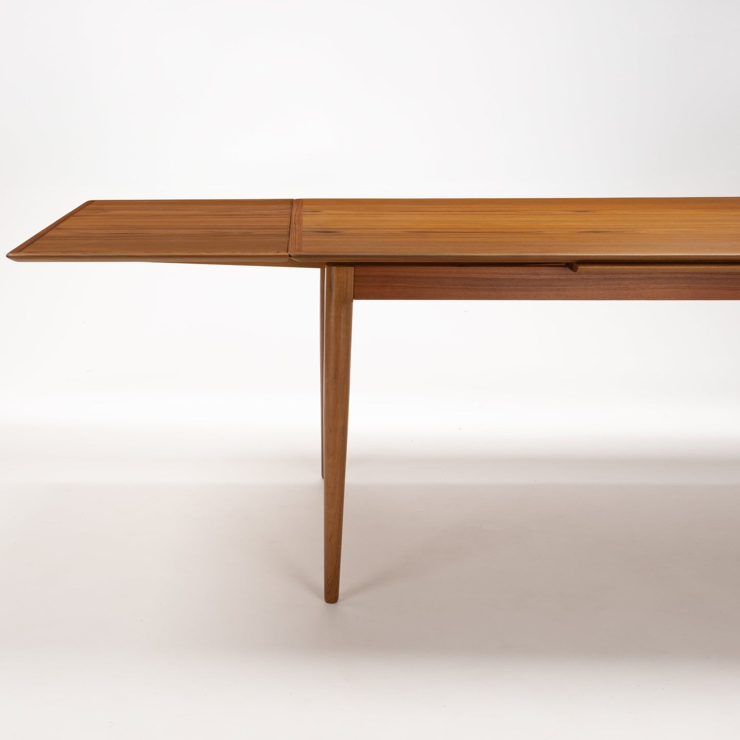 Danish Draw-Leaf Dining Table in Teak with an extended leaf rich linear wood grain and slender tapered leg in vintage Danish furniture style