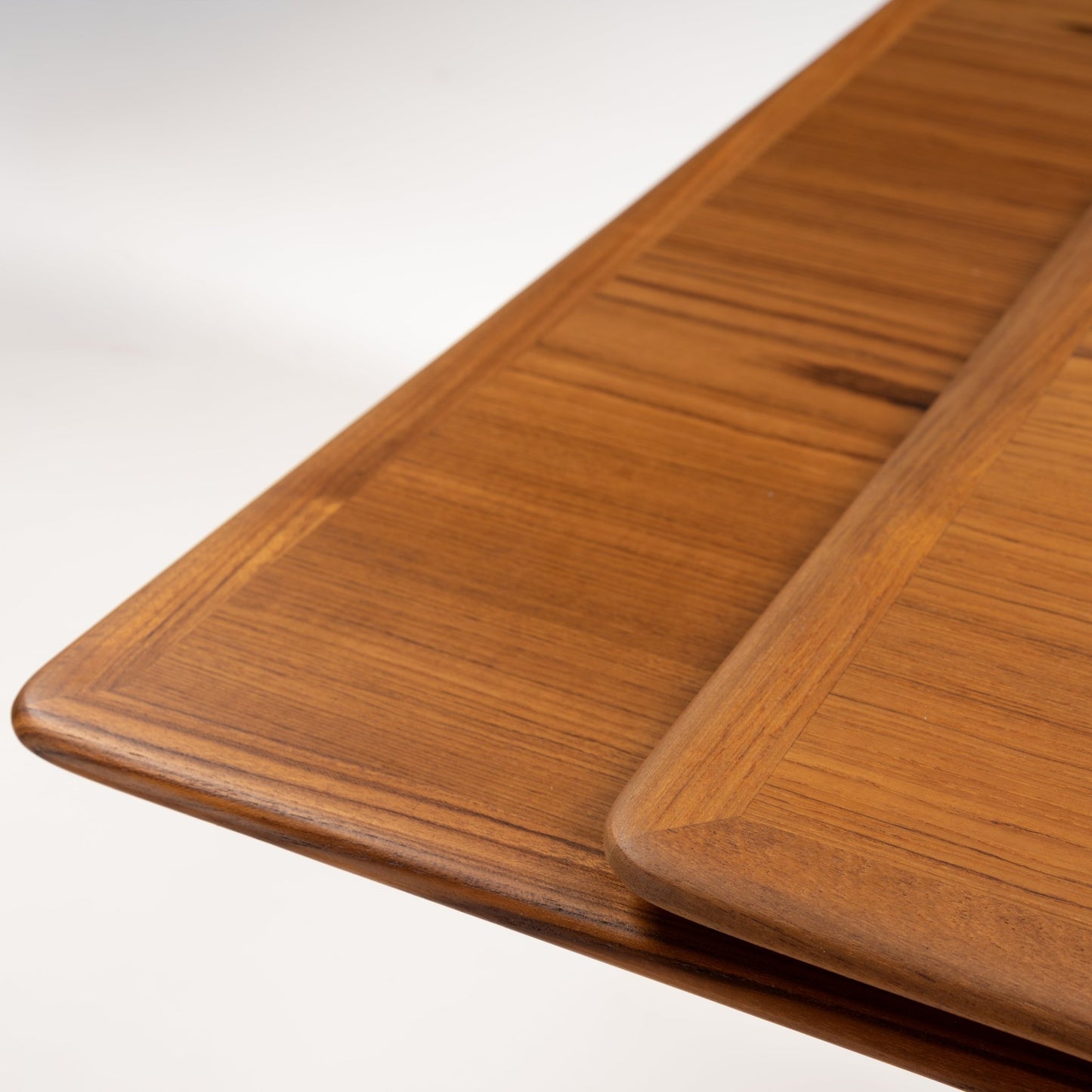Danish Draw-Leaf Dining Table in Teak featuring warm linear wood grain a rounded edge and overlapping extension leaf in vintage Danish furniture style